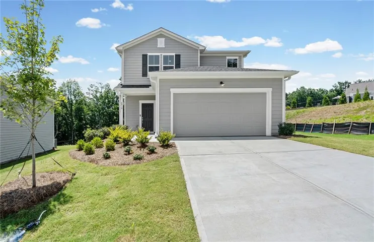 Gray siding exterior with dark shutters, attached two-car garage, concrete driveway, and established front landscaping