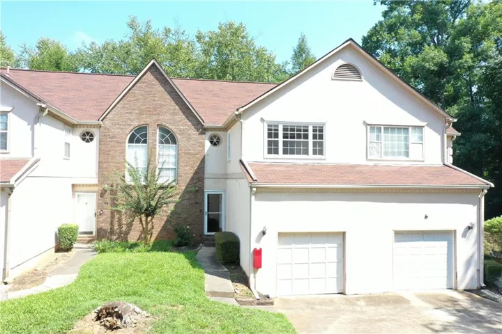 Brick and stucco townhouse exterior featuring arched windows, round accent windows, a gable roofline, and dual garage doors
