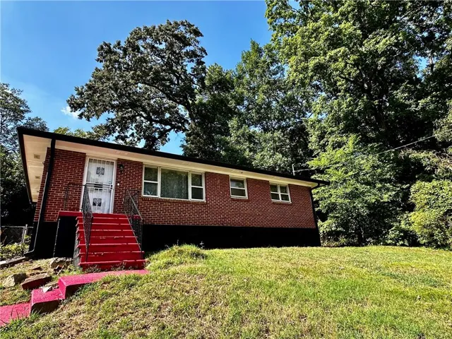 Brick exterior with multiple windows, prominent red stairs, and established trees