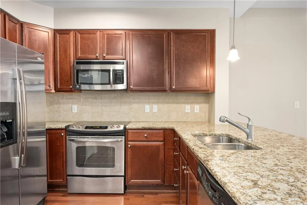 Kitchen with backsplash, decorative light fixtures, sink, and appliances with stainless steel finishes