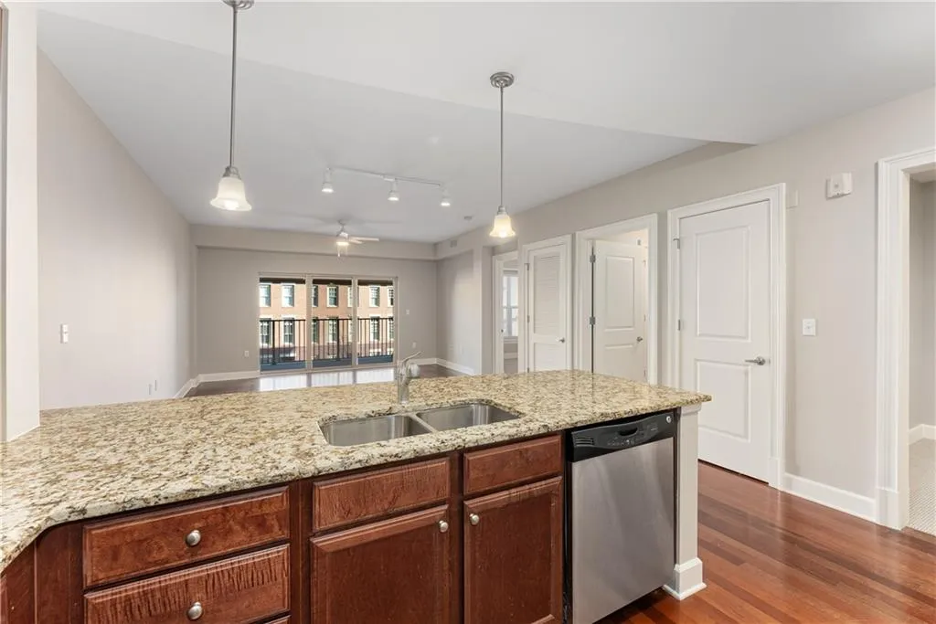 Kitchen featuring hanging light fixtures, light stone counters, sink, and stainless steel dishwasher