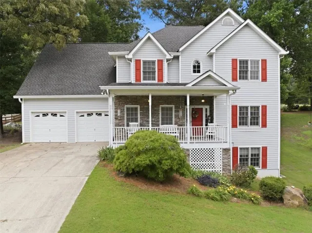 Two-story residence featuring light gray siding, a covered front porch with stone accents, a two-car garage, and a concrete driveway