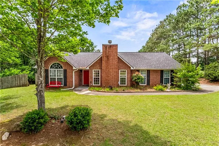 Brick exterior residence featuring an arched window, a prominent brick chimney, and a dark shingle roof