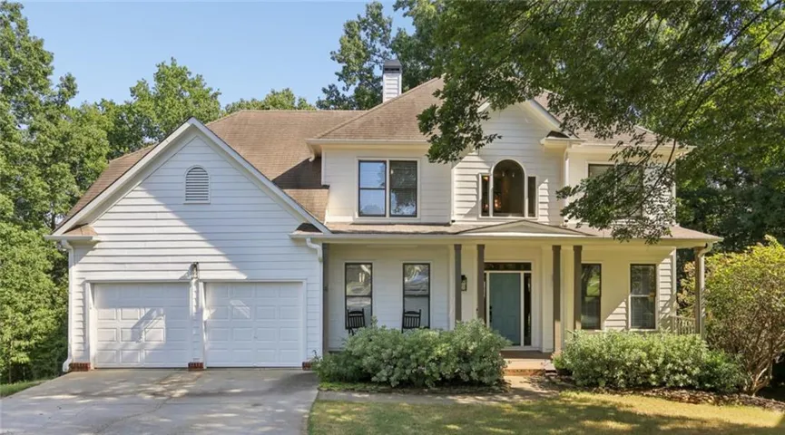Two-story exterior with white siding, a two-car garage, and a covered front porch with dark pillars