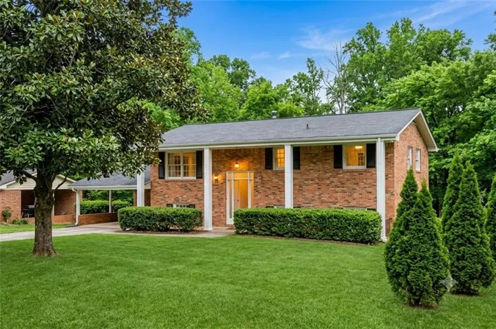 Brick exterior featuring white columns, black shutters, and a dark roof