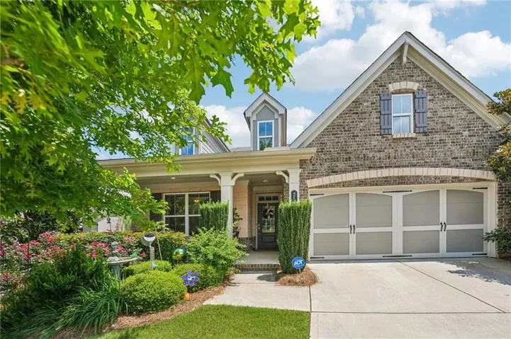 Brick facade home featuring a two-car garage with arched decorative doors, a covered front porch with white columns, and a dormer window