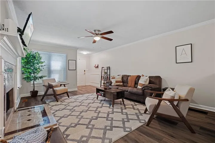 Living area featuring wood-finish flooring, a ceiling fan with integrated lighting, crown molding, and a fireplace with a tiled hearth