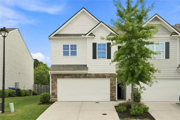 White siding exterior with a stacked stone accent, attached garage, and a concrete driveway