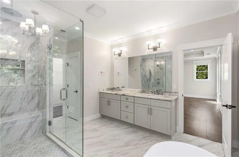 Bathroom with a marble finish shower, a chandelier, double vanity, ornamental molding, and light marble finish floors