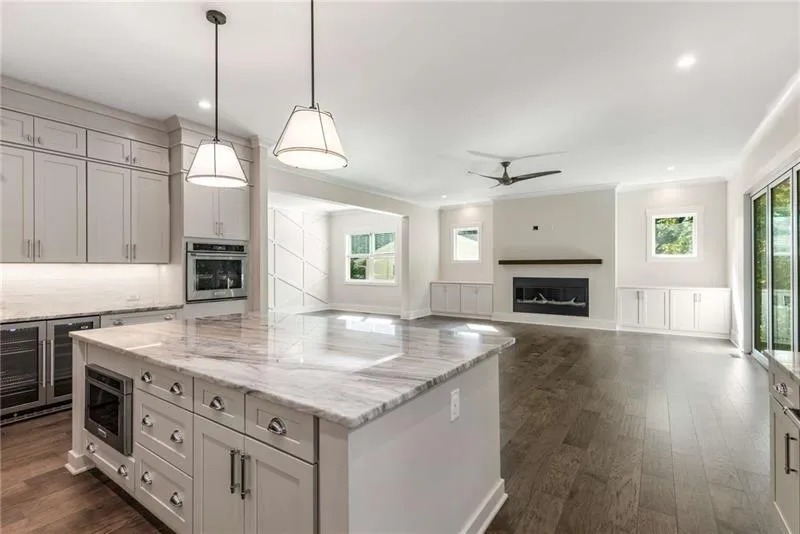 Kitchen with dark wood-style flooring, pendant lighting, a center island, light stone countertops, and beverage cooler
