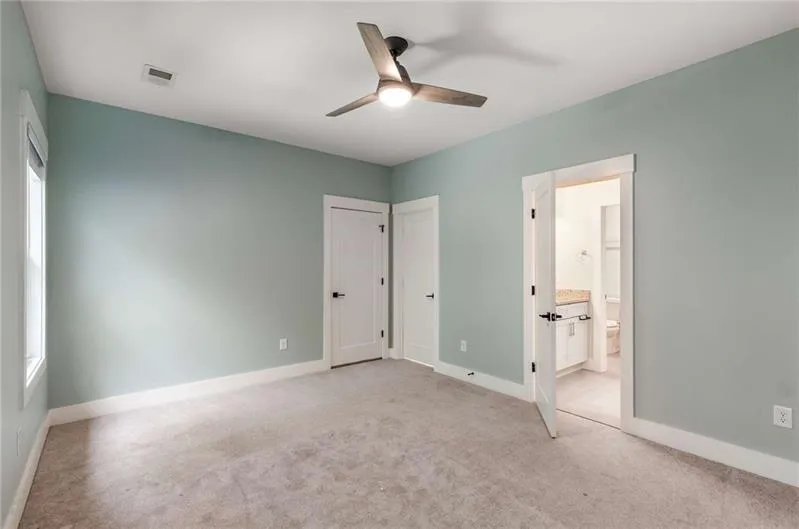 Unfurnished bedroom featuring light carpet, ceiling fan, and ensuite bathroom