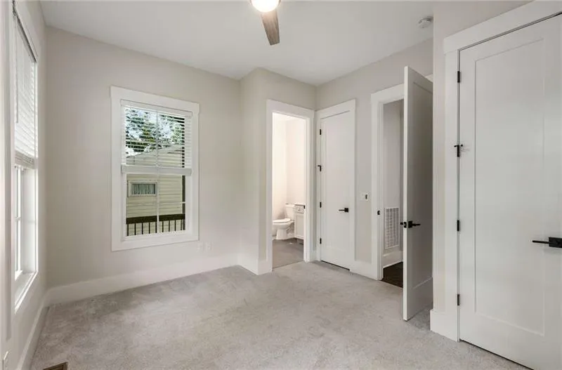 Unfurnished bedroom featuring light colored carpet, ensuite bathroom, and ceiling fan