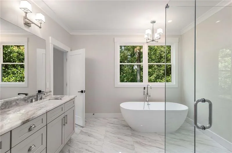Full bathroom featuring vanity, crown molding, a freestanding tub, light marble finish floors, and a shower stall