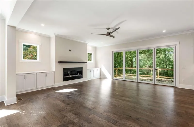 Unfurnished living room with plenty of natural light, a glass covered fireplace, crown molding, ceiling fan, and dark wood-type flooring