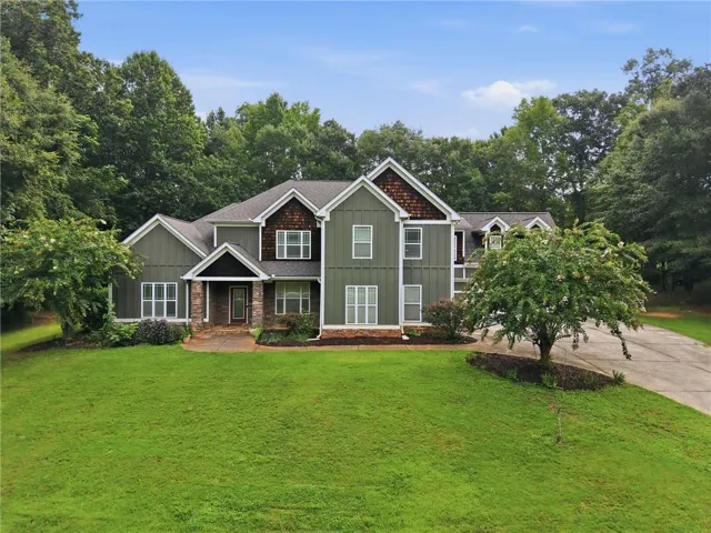 Expansive residence featuring a multi-gabled roof, board and batten siding, stone accents, a covered front entry, and a paved driveway