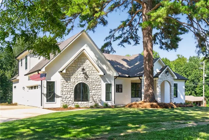White stucco exterior featuring a stone accent façade, arched stone entry, and a prominent mature tree