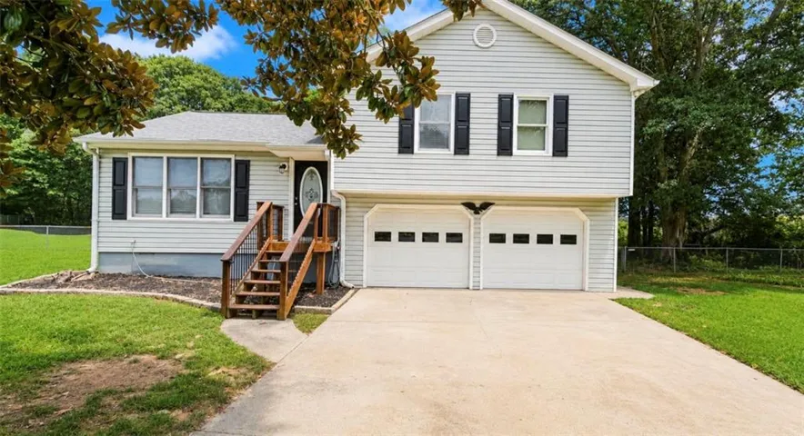 Split-level residence featuring light-colored siding, black window shutters, a two-car garage with panel doors, and a concrete driveway
