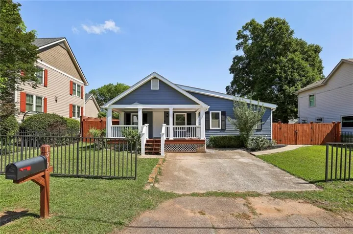 Blue-sided residence featuring a covered front porch with white railings, a concrete driveway, and a front yard with wrought iron fencing