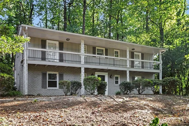 Two-story residence featuring a brick and siding exterior, upper-level balcony, lower-level porch, and mature trees surrounding the property
