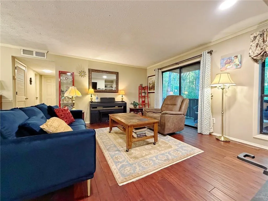 Living room with dark wood-style flooring, a textured ceiling, a glass covered fireplace, ornamental molding, and recessed lighting