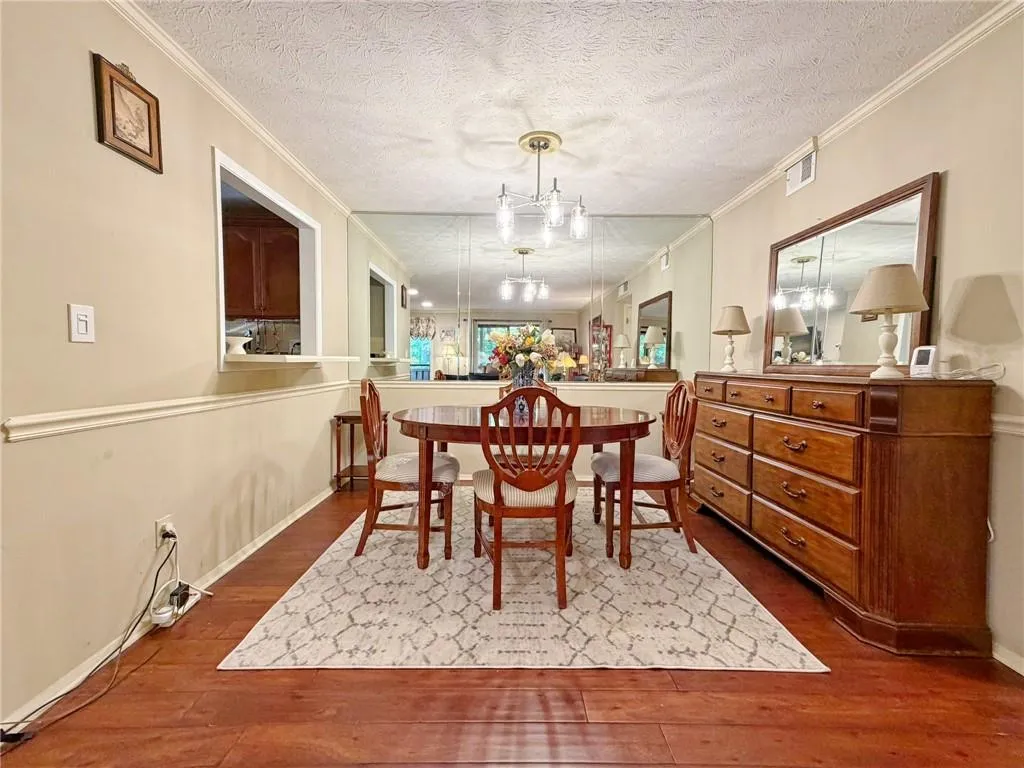 Dining space featuring a textured ceiling, dark wood-type flooring, ornamental molding, and hanging lights