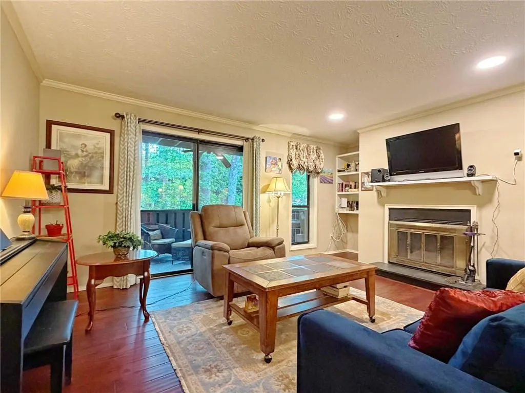 Living room with dark wood-style flooring, a textured ceiling, a glass covered fireplace, ornamental molding, and recessed lighting
