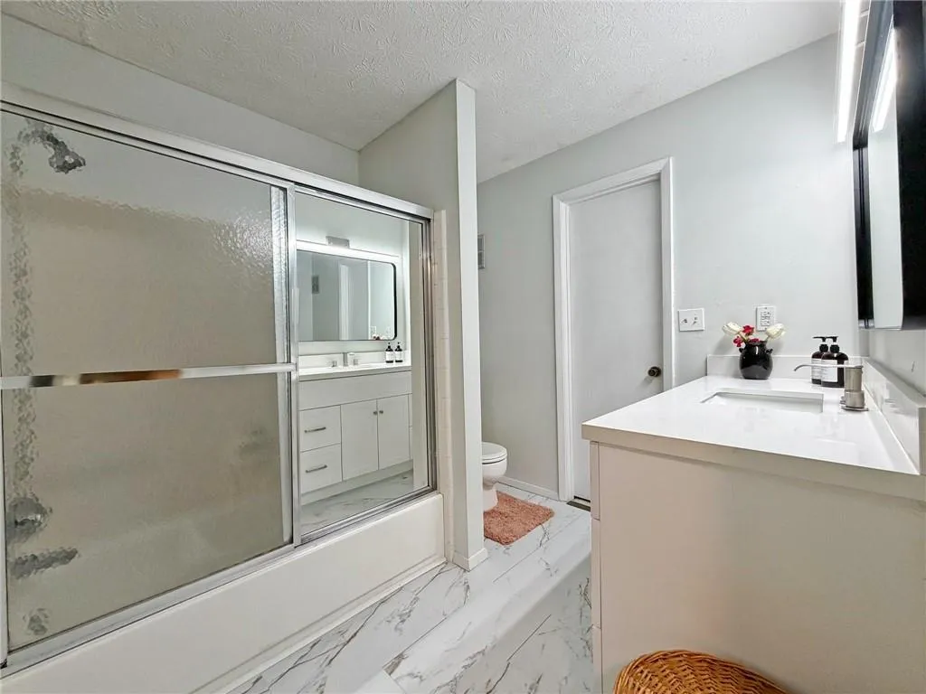 Full bathroom with vanity, combined bath / shower with glass door, a textured ceiling, and light marble finish floors