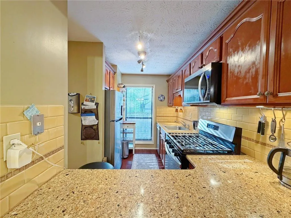 Kitchen with stainless steel appliances, decorative backsplash, light stone countertops, and a textured ceiling