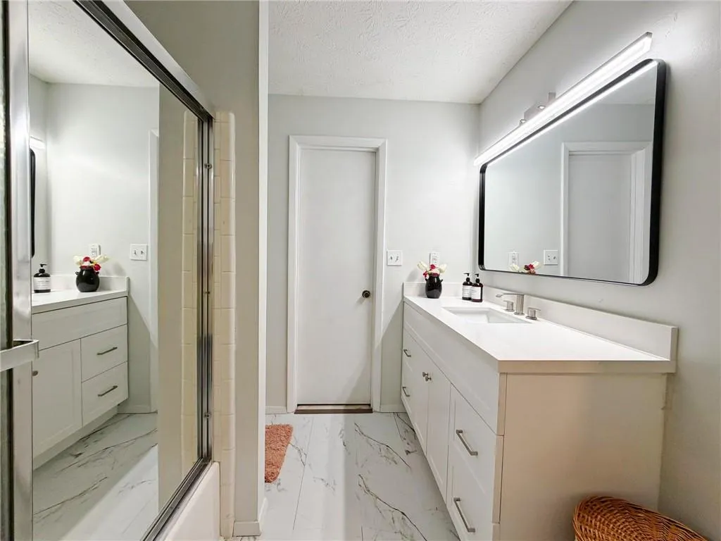 Bathroom featuring vanity, a shower with door, light marble finish flooring, and a textured ceiling