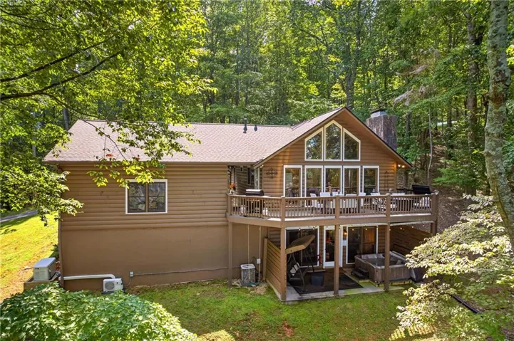 Two-story residence featuring a wood-sided exterior, expansive deck with railing, floor-to-ceiling windows, and a lower-level patio