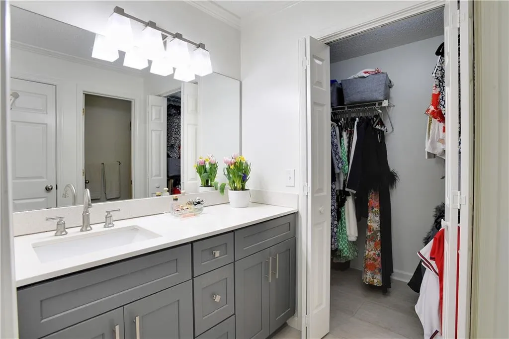The updated guest bath features a single quartz vanity with an under mounted sink. The oversized walk-in closet is in the background.