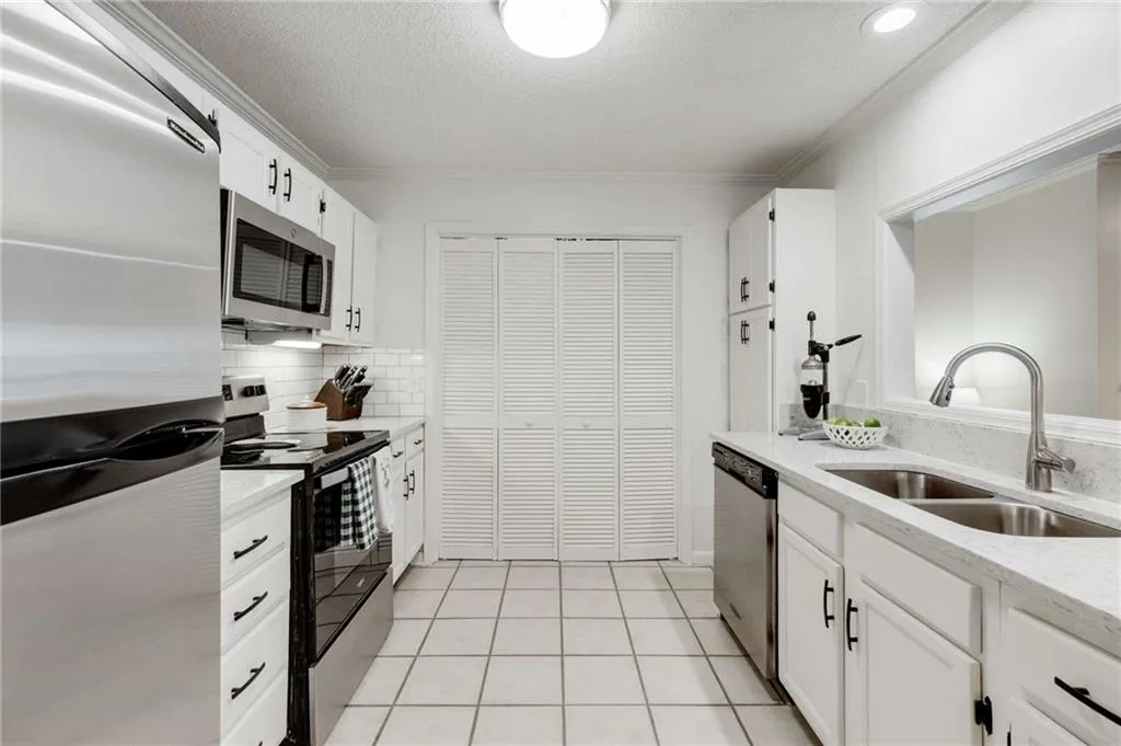 The kitchen feautres stainless steel appliances, white quartz counters, tile flooring, white cabinetry & a pass through window breakfast bar.