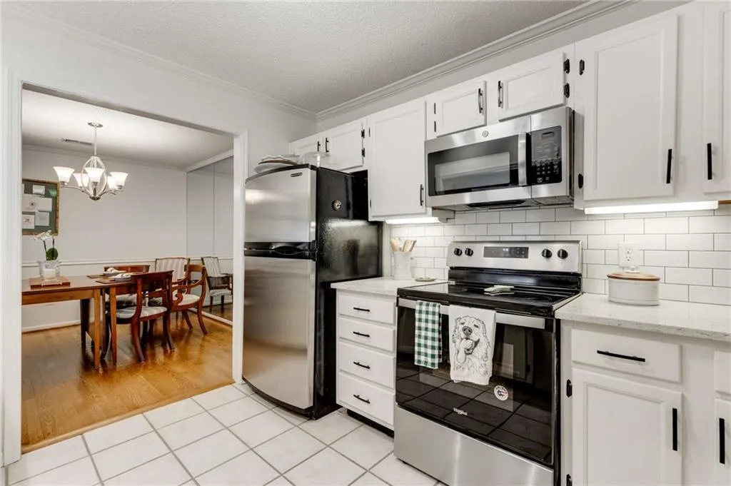 Another view of the updated gourmet kitchen featuring plentiful cabinetry, stainless appliances, quartz counters & custom tile backsplash with a view into the separate dining room.