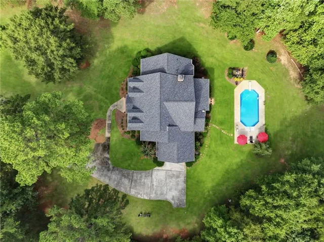 Expansive green lawn surrounds the property, featuring a multi-gabled roofline, a curved concrete driveway, and a rectangular swimming pool with integrated steps
