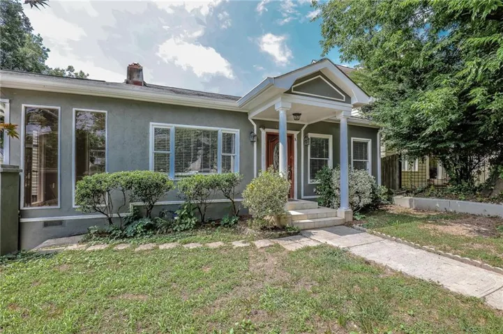 Stucco exterior with a covered front entry, prominent columns, bay window, and a concrete pathway
