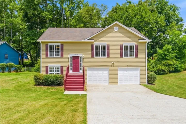 Split-level residence featuring yellow siding, a red entry door, and a two-car garage