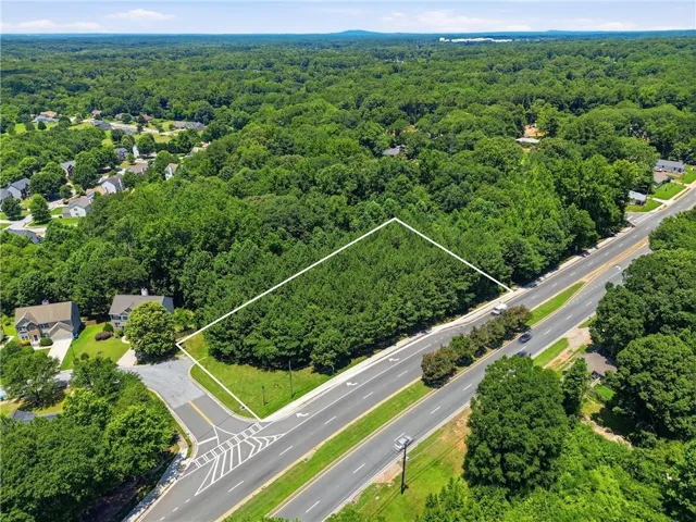Wooded parcel with road frontage, bordered by a paved street and a residential area