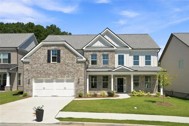 Brick and siding exterior with a covered front porch, a two-car garage, a concrete driveway, and a manicured front lawn