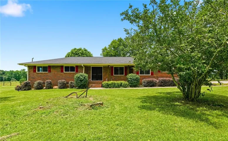 Brick residence featuring a dark shingle roof, red window shutters, and a covered entry