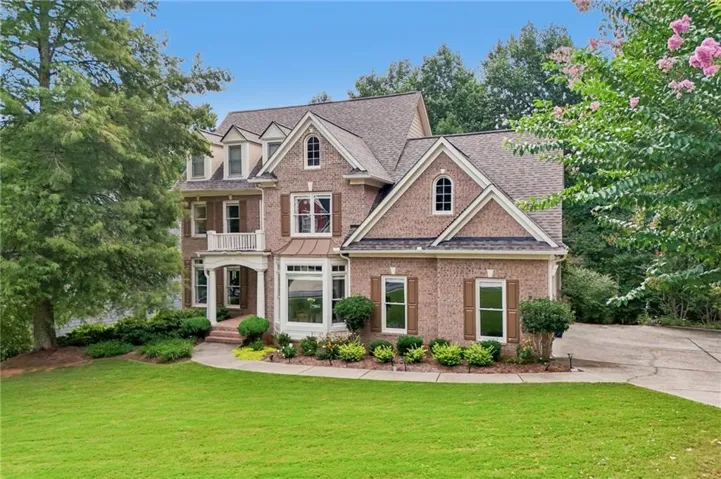 Brick exterior residence featuring multiple dormer windows, a bay window with a copper-tone awning, and a balcony with white railings