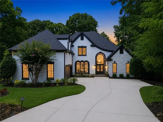 Modern stucco and stone facade featuring a prominent arched entry, black-framed windows, and a black shingle roof