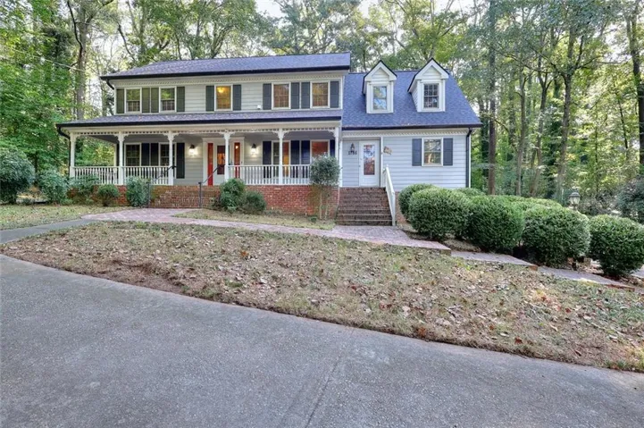 Two-story residence with a covered front porch featuring white railings, light-colored siding, and a dark shingle roof