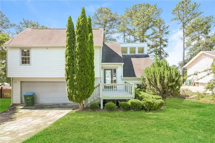 White siding exterior with a two-car garage, upper-level deck, and mature landscaping