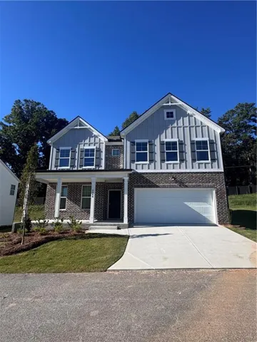 Two-story residence featuring a brick and board-and-batten exterior, an attached two-car garage, a covered front porch, and a concrete driveway