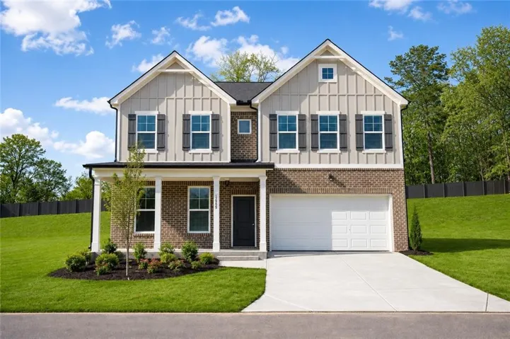 Two-story residence featuring a brick and board-and-batten facade, a covered front porch with white columns, a two-car garage with a concrete driveway, dark shutters, and a landscaped front yard