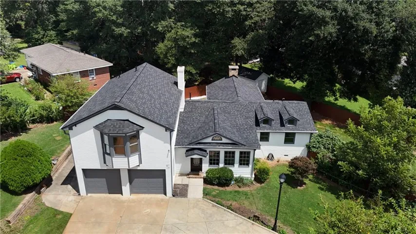 White exterior with a dark shingle roof, featuring dormer windows, an attached two-car garage, a bay window, and mature landscaping