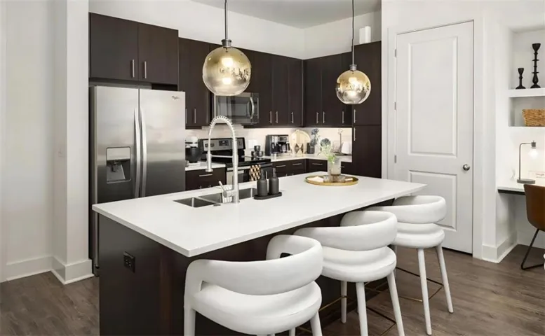 Kitchen featuring dark hardwood / wood-style floors, a kitchen breakfast bar, a center island with sink, stainless steel appliances, and dark brown cabinetry
