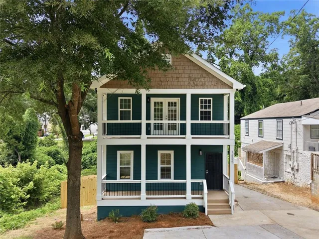Two-story residence featuring teal siding with white trim, a wood-shingle gable, and a two-tiered porch with white railings
