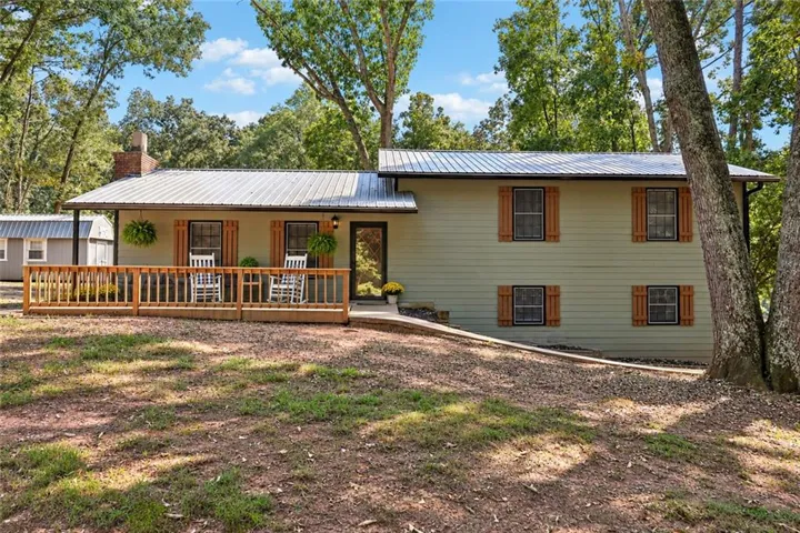 Light green exterior siding with wood shutters, front porch with wooden railing, metal roof, and brick chimney