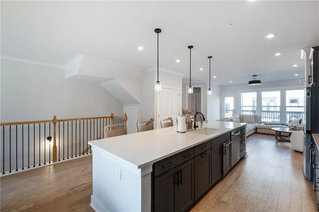 Kitchen with open floor plan, light wood finished floors, ornamental molding, hanging light fixtures, and a kitchen island with sink